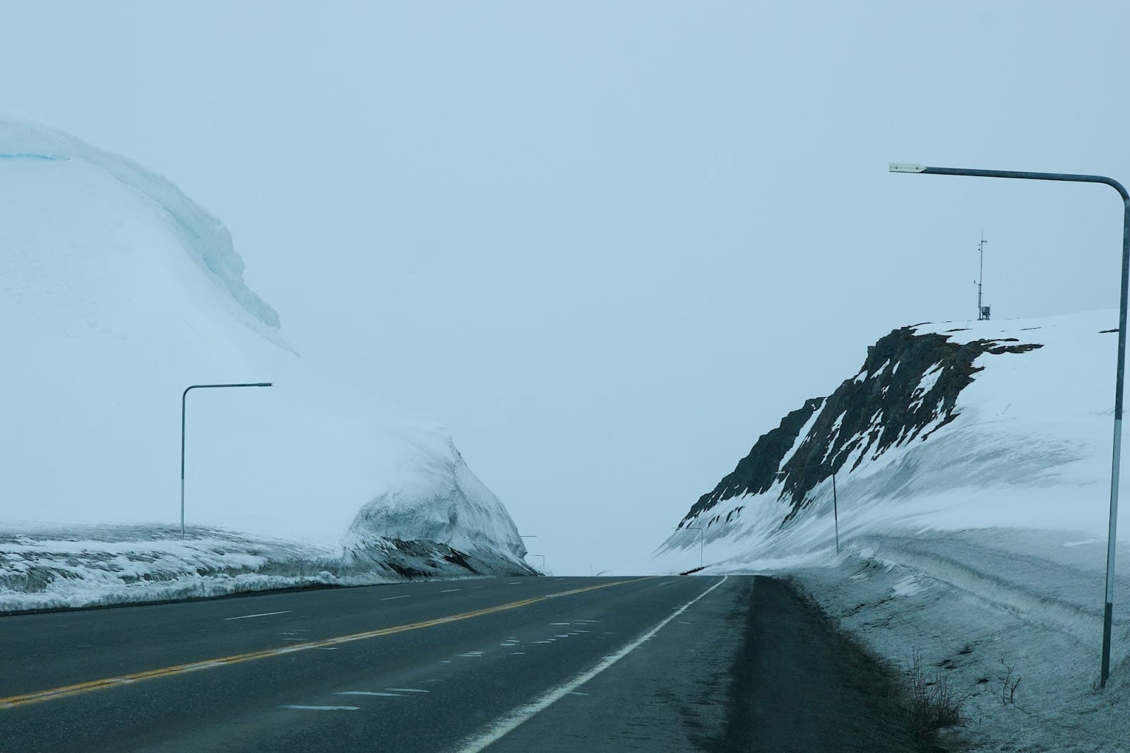 Road winds through snow-covered mountains under overcast skies.